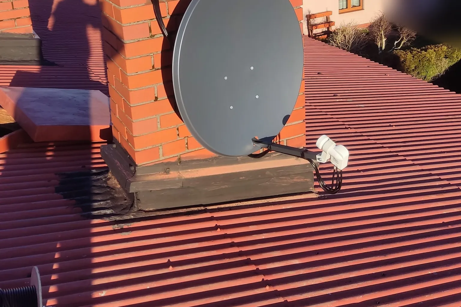 Antena satelitarna przy kominie na dachu pokrytym blachą