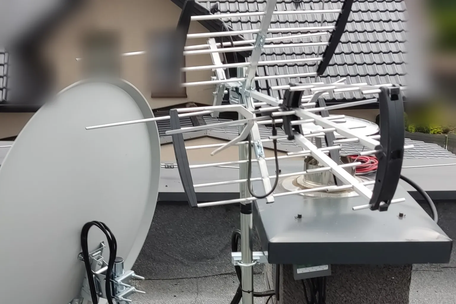 Antena DVB-T2 i czasza satelitarna na maszcie przy kominie na płaskim dachu